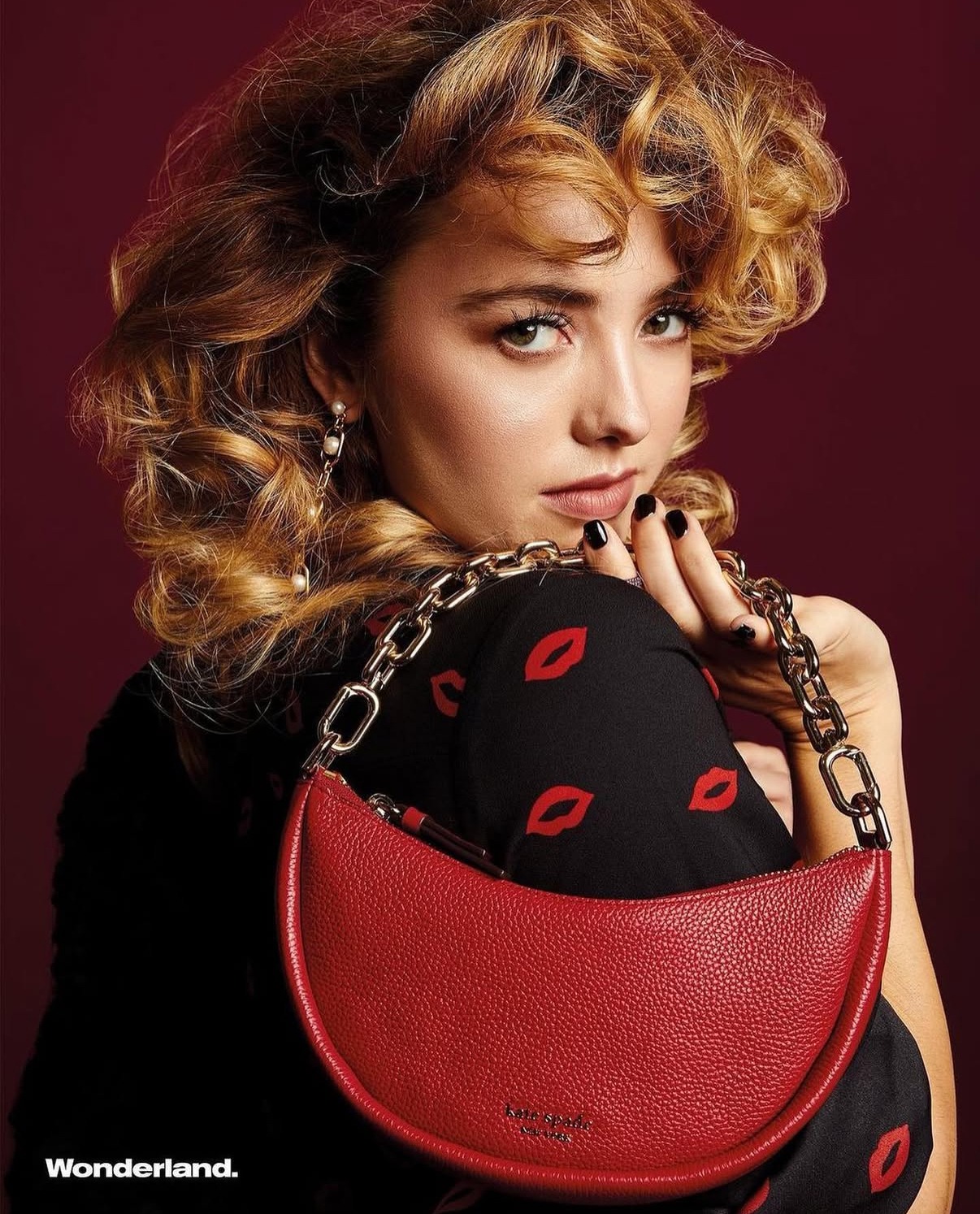 Peyton List of Cobra Kai in a black lip-print top with a red handbag for Wonderland's Kate Spade collaboration
